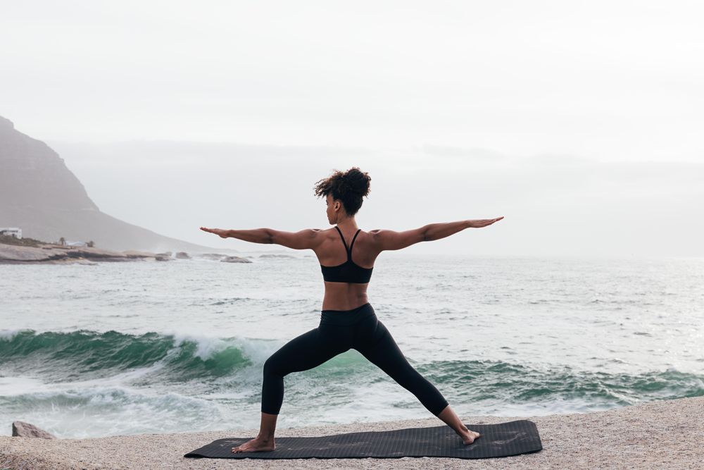 Back of female stretching with open arms while facing the ocean