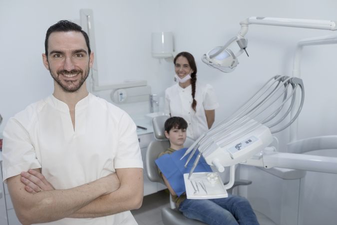 A portrait of a smiling dentist with his team smiling with teenage patient in the background