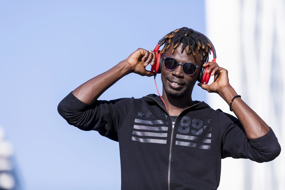 Black man wearing headphones & sunglasses standing on the street listening to music