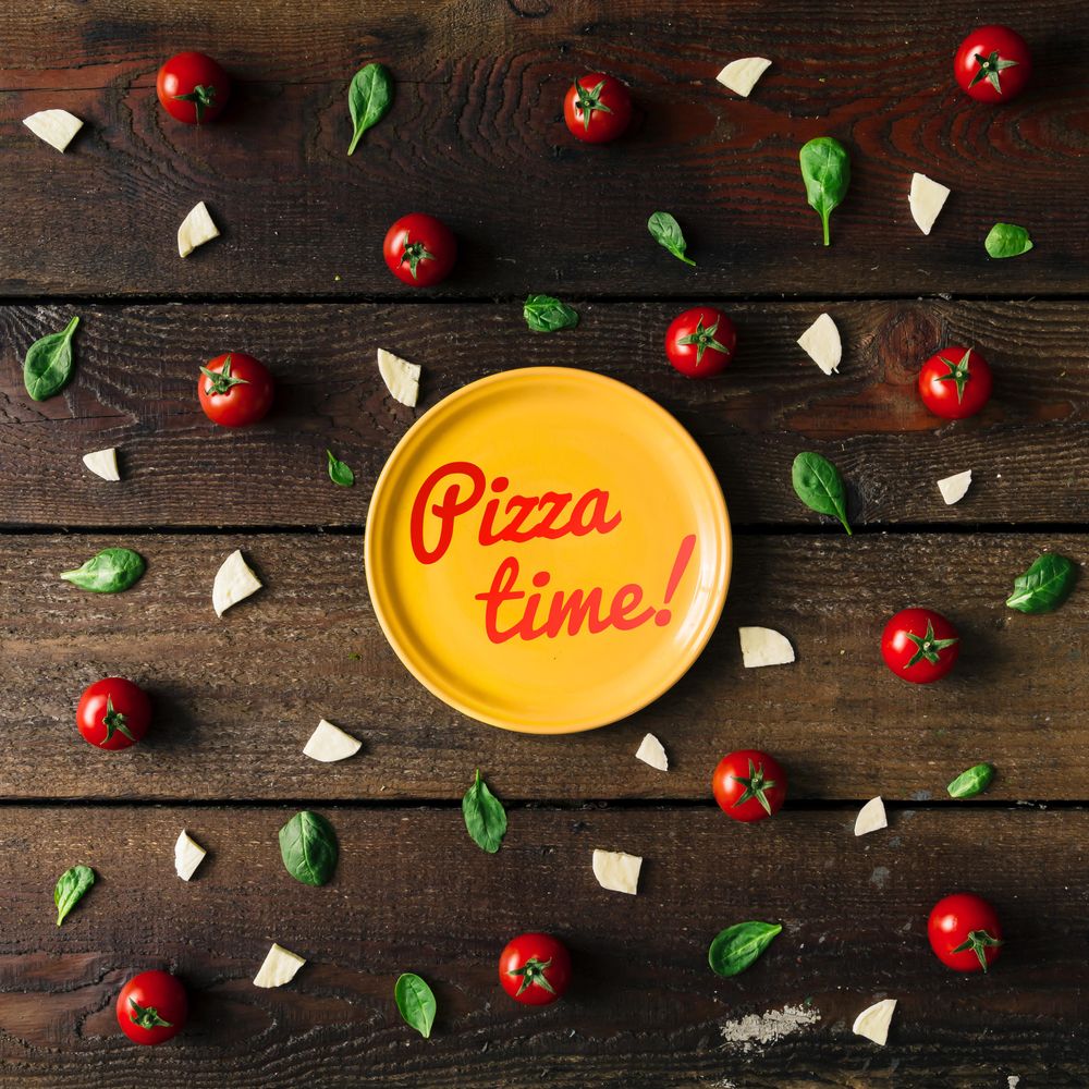 Basil, tomatoes, and cheese on wooden background with plate and “Pizza time!” text