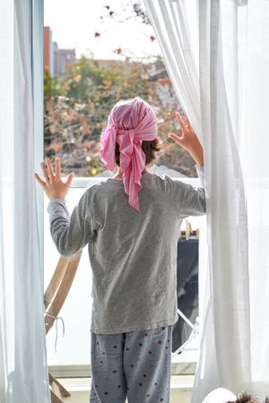 Kid with pink headband looking out glass door at home