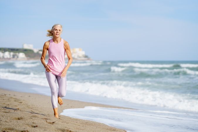 Healthy mature woman in sports gear jogging along beach