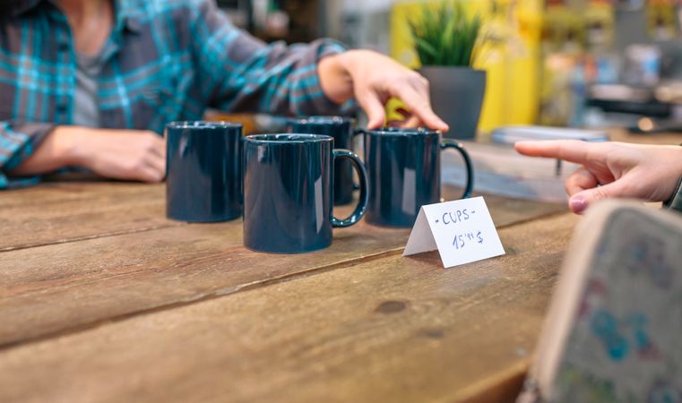 Unrecognizable female customer pointing with her finger blue mug to buy on local store