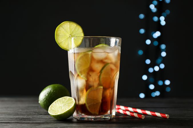 Glass of cold cola with citrus and ice on wooden table against dark background