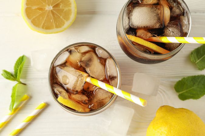 Glasses with cold cola and citrus on wooden background, top view