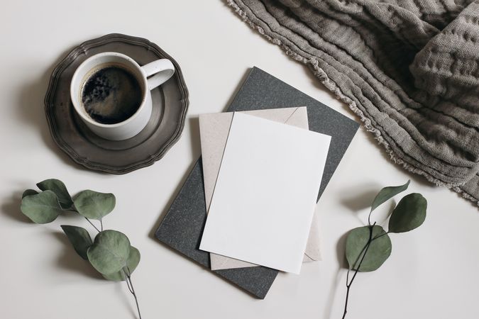 Blank greeting card, invitation mockup, dry eucalyptus tree branches, diary and linen blanket with cup of coffee