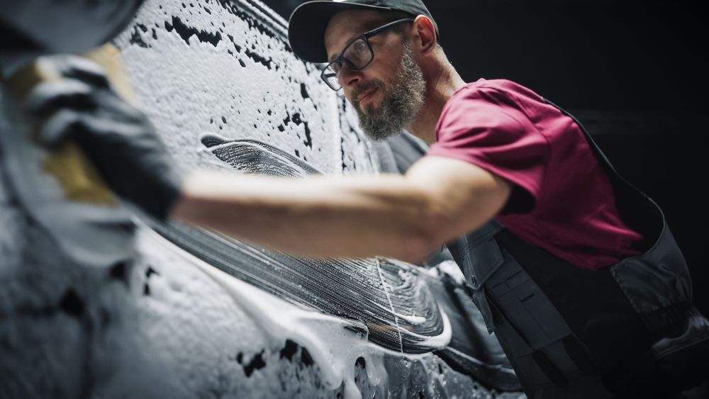 Portrait of an Adult Man Working in a Detailing Studio, Prepping a Factory Fresh Electric SUV for Maintenance Work and Car Care Treatment.