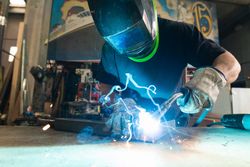 Welder in protective helmet welding metal detail in workshop