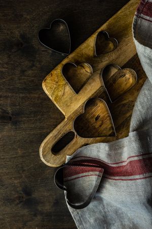 Heart shaped cookie cutters on wooden cutting board with kitchen towel