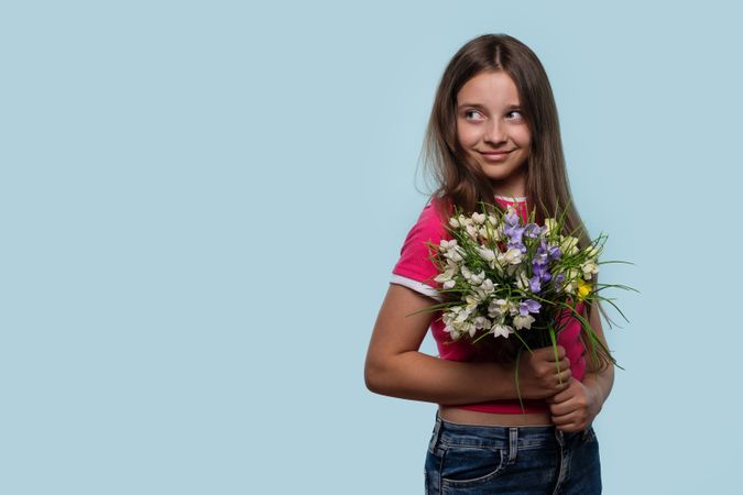 Girl smiles mischievously while holding colorful bouquet of flowers.