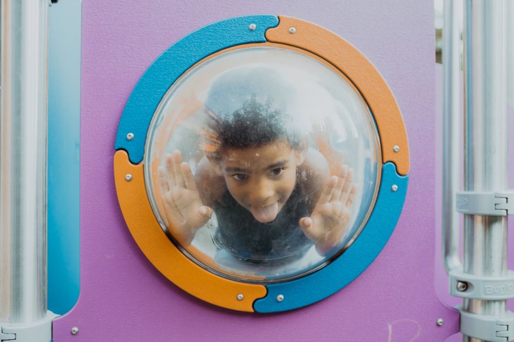 Funny Black boy behind porthole on playground