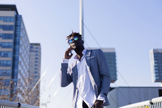 Black man in elegant suit standing in city talking on phone on a sunny day