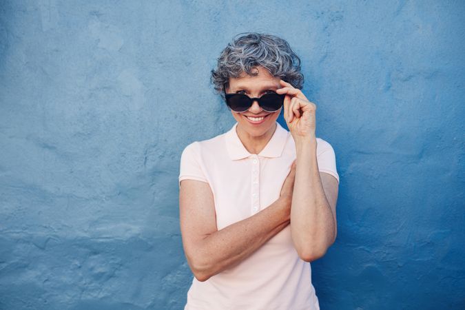 Portrait of smiling mature woman peeking over sunglasses