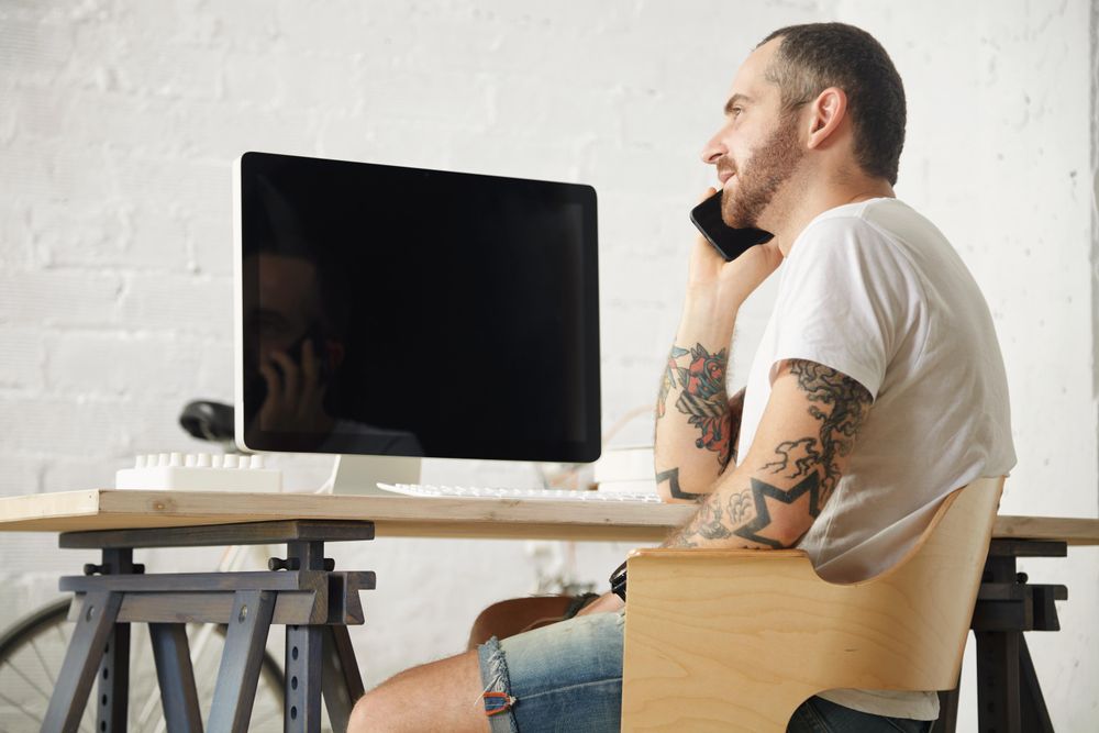 Tattooed man in blank t-shirt speaking on mobile phone