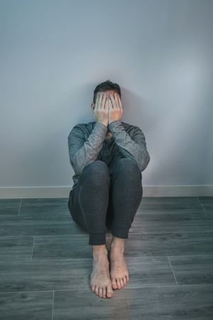 Man crying while covering his face with hands sitting on the floor