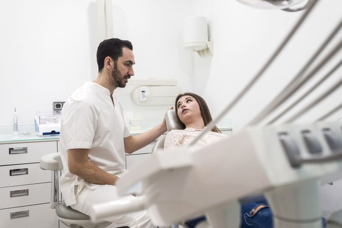 Portrait of a bearded dentist explaining procedure to a female teenage patient