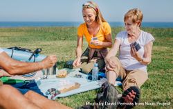 Smiling family playing card game during a picnic near the ocean 5QGlnb