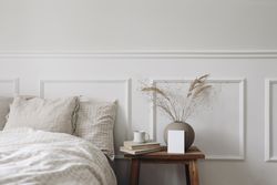 Bedside table with mockup frame and vase next to comfortable bed