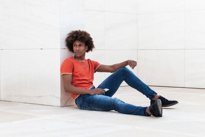 Concentrated young man sitting on floor and holding smartphone