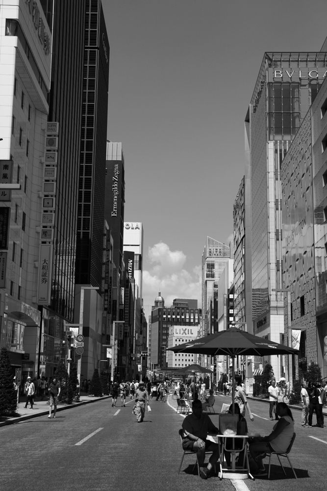 Grayscale photo of people sitting at a table in the middle of the road
