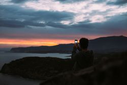 Male with smartphone overlooking the ocean at dusk