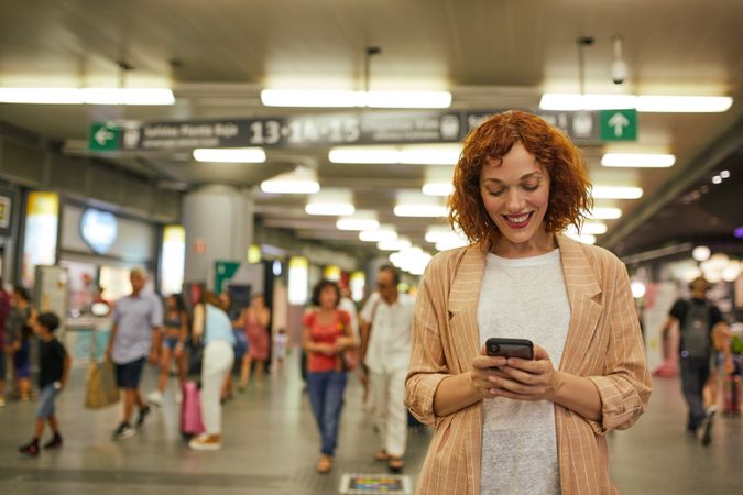 Red haired young woman using smartphone at station
