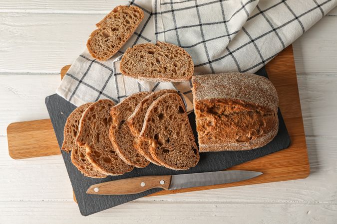 Composition with bread, knife, kitchen towel and cutting board on wooden background, top view and space for text