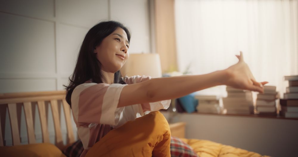 Korean Woman Waking up in the Morning, Doing some Stretching, Appreciating the Sun Shining Through her Window.