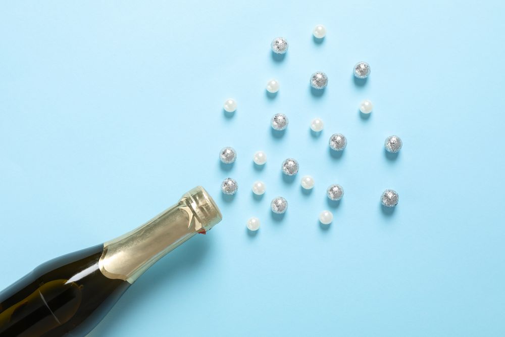 Champagne bottle and glitter on blue background, space for text