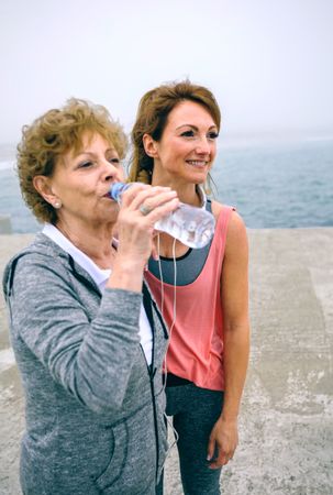 Older sportswoman drinking water with female coach