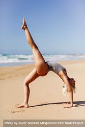 Woman doing bridge with leg stretched above on sand on a Spanish beach 5qeWa5