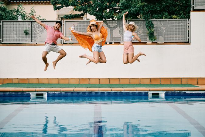 two young women and a man jumping by the pool