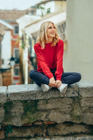 Blond woman smiling and sitting on stone wall with legs crossed