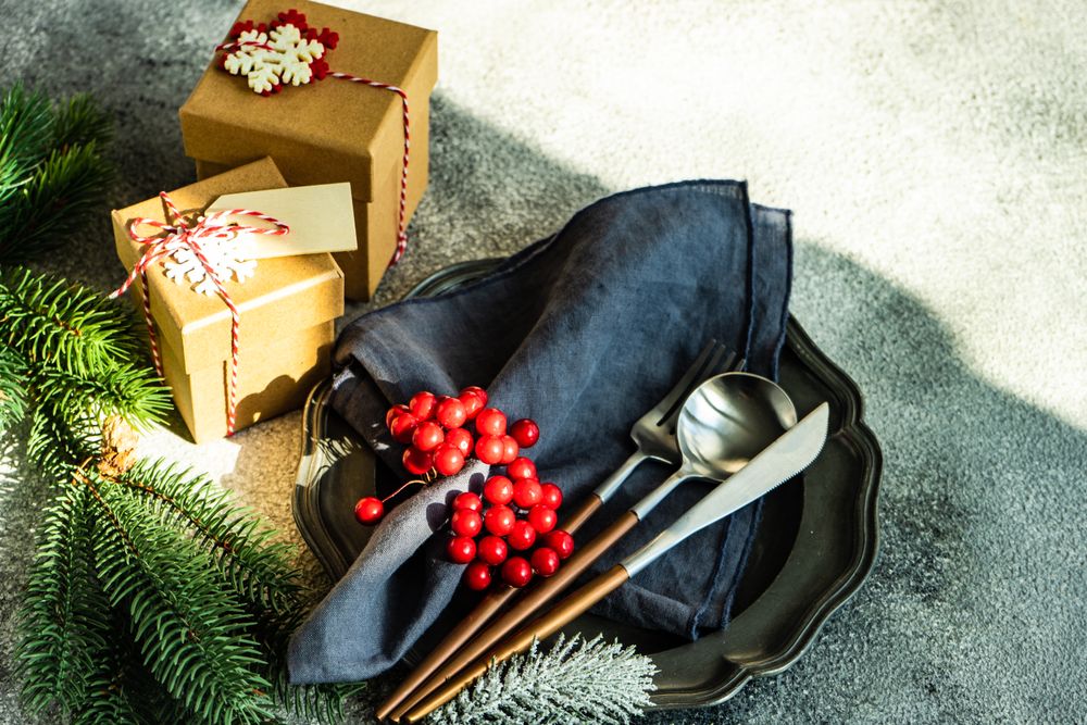 Christmas gifts with pine and gingerbread ornament next to dark plate and cutlery
