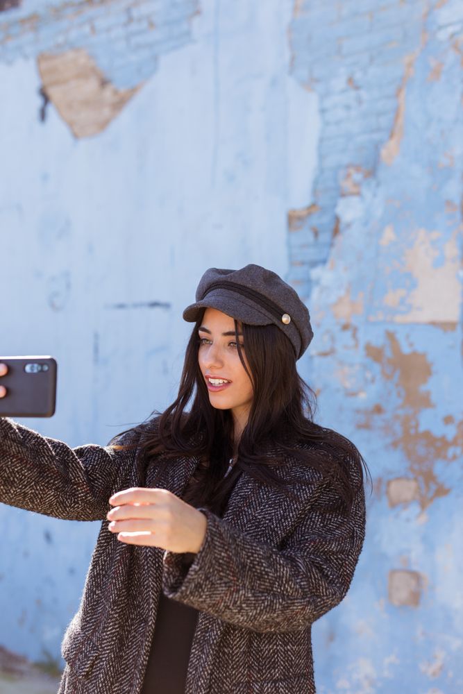 Charming Hispanic woman taking selfie near wall