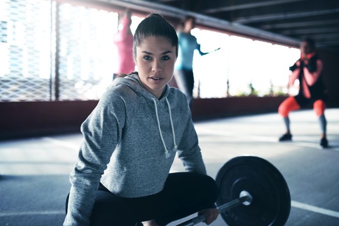 Portrait of woman about to with heavy barbell with others working out in the background