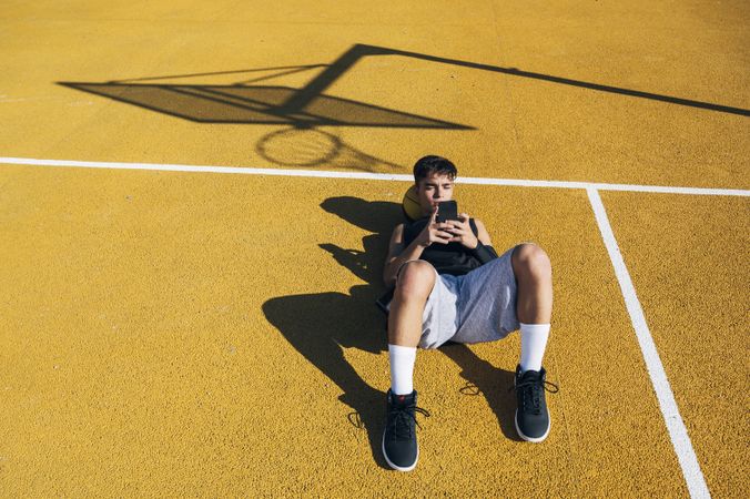 Male basketball player using his smartphone resting after training
