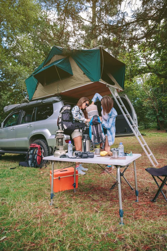 Young women in campsite packing blanket inside backpack