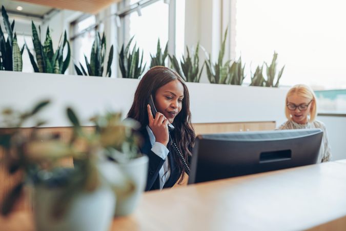 Two woman working behind a front desk with plants