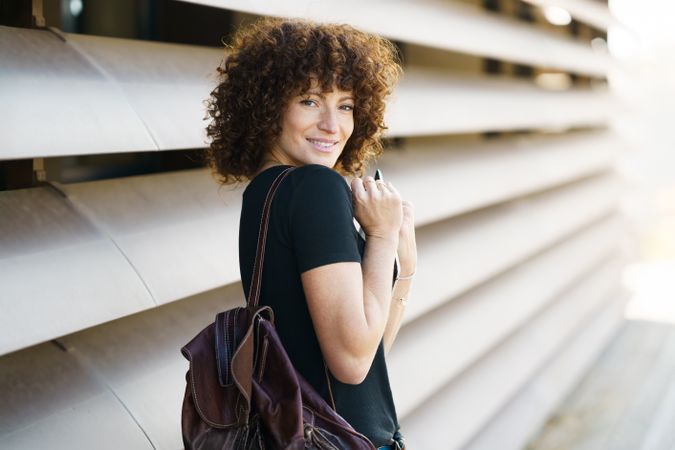 A young woman smiles outdoors with a backpack, embodying a cheerful spirit in a vibrant setting