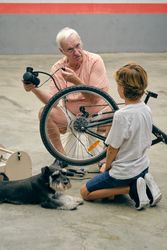 Grandfather pumping up bicycle wheel with grandson near dog