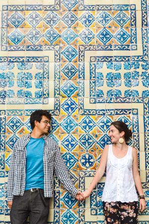 Smiling man holding hands with smiling woman while leaning on wall