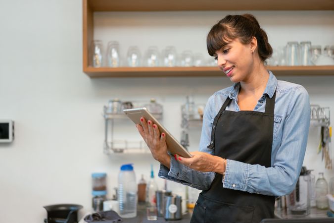 Smiling female coffee shop owner wearing apron using digital tablet
