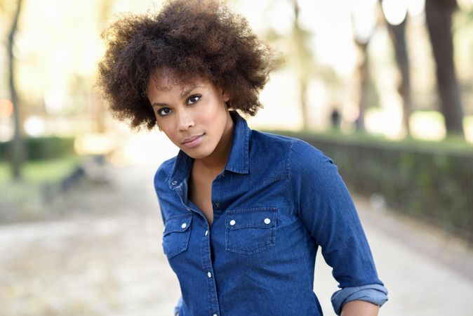 Serious woman standing outside in denim shirt looking at camera