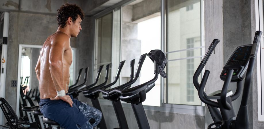 Muscular male working out on cycling machine at gym