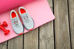 Karemat, sneakers and dumbbells on wooden background, space for text