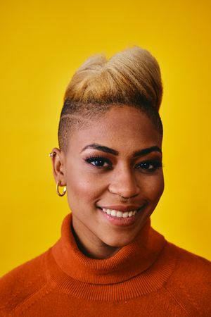 Studio shot of smiling Black woman with short blonde hair in orange sweater