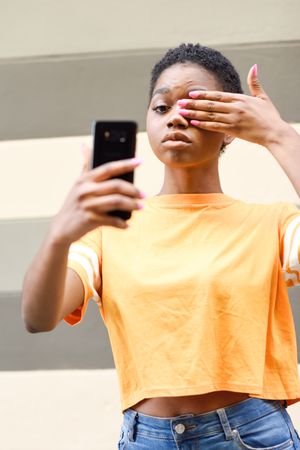 Female taking funny photo with one eye covered in front of striped wall