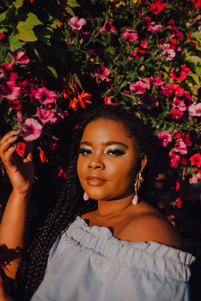 Joyful trendy Black woman standing beside blossomed tree