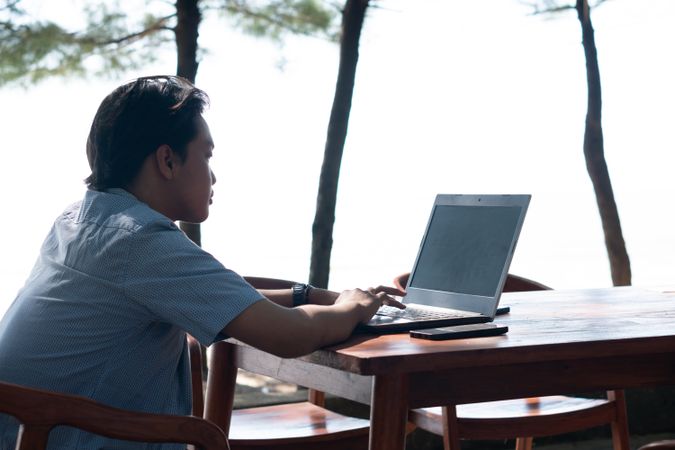 Back View Asian Young businessman work at outdoor with laptop blank screen. Concept of remote and freelance work. Young successful man wearing casual blue cloth.